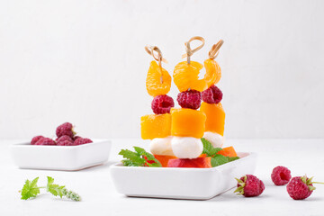Fruit skewers with mango, tangerine, peach, raspberry and mozzarella on the white table. Healthy...