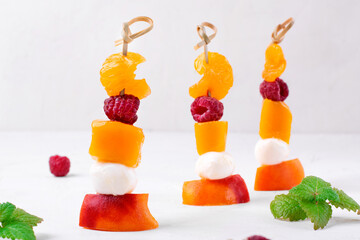 Fruit skewers with mango, tangerine, peach, raspberry and mozzarella on the white table. Healthy summer dessert. Party food