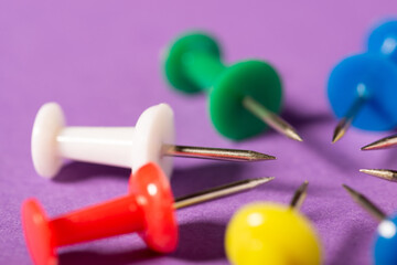 Pins in a circle pointing to one spot. Drawing pins of different colours on violet background
