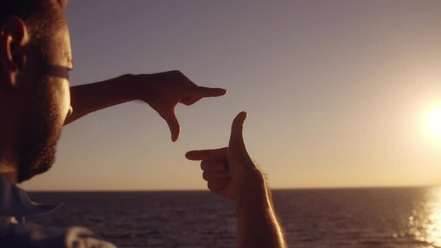 Male photographer making finger frame gesture to make beautiful seascape shot
