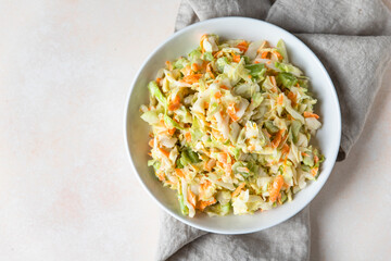 Coleslaw. Salad made of shredded white cabbage, grated carrot and rhubarb with orange mayonnaise dressing in white bowl, light concrete background.