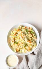 Coleslaw. Salad made of shredded white cabbage, grated carrot and rhubarb with orange mayonnaise dressing in white bowl, light concrete background.