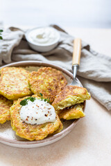 Vegetable fritters or pancakes with yoghurt or cream sour dressing and herbs. Cabbage or zucchini fritters on ceramic plate. Healthy vegetarian food.