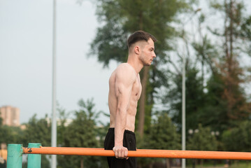 Young attractive Caucasian man doing push ups on the bars. Workout concept