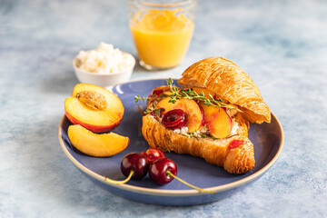 Fresh croissant with cream cheese, nectarine and cherry on blue ceramic plate on a blue background. Breakfast with croissant and juice.