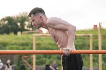 Young attractive Caucasian man doing push ups on the bars. Workout concept