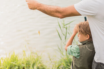 A boy learns how to fish under the guidance of an adult