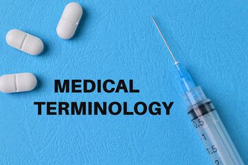 Syringe injection and pill capsules on blue background with text MEDICAL TERMINOLOGY - obrazy, fototapety, plakaty