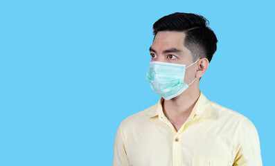 Terrible headache. COVID-19 Coronavirus close up handsome young asian man wearing yellow shirt and mask protection from covid 19 isolated on blue background in studio. Asian man people.