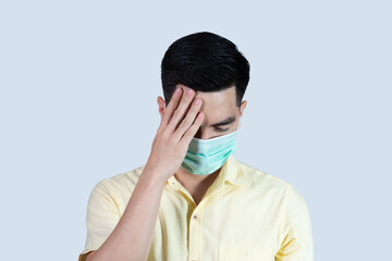 Terrible headache. COVID-19 Coronavirus close up handsome young asian man wearing yellow shirt and mask protection from covid 19 isolated on grey background in studio. Asian man people.
