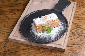 Freshly baked apple pie with apples, mint leat and powdered sugar. Served on a black plate over wooden background.