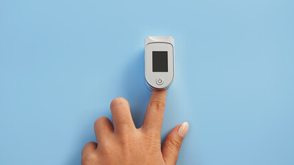 Medical device for hypoxia. Female finger in a pulse oximeter on a blue background with copyspace