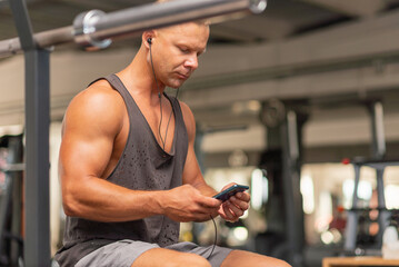 Man in gym using smartphone with headphones sportsman in headphones choose music on his smartphone at gym.