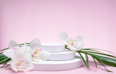 Fototapeta na wymiar White geometric shapes podium for product display on pink background with orchid flowers and palm leaves. Monochrome stage, stand for product promotion in minimal style.