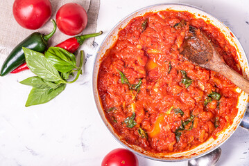 Hot sauce for pasta and pizza in a frying pan on the table with ingredients - tomatoes, basil and hot peppers, top view, copy space