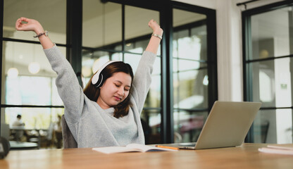 A woman stretches her arms above her head to relieve fatigue while working on her laptop.