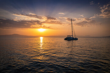 Beautiful sunset behind the mediterranean sea with a sailing boat and calm, reflecting sea as seen in Peloponnese, Greece