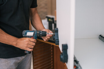 Man attaching a piece in a furniture using a drill in a workshop