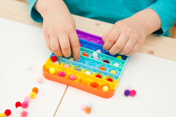 Child plays with sensory fidget toy Pop-it. Instrument for fine motoric skils, tool to start...