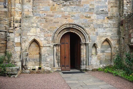 Arched doorway with half open door in ancient medieval European stone wall