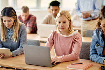 Young student uses laptop while attending class with her friends at university classroom.