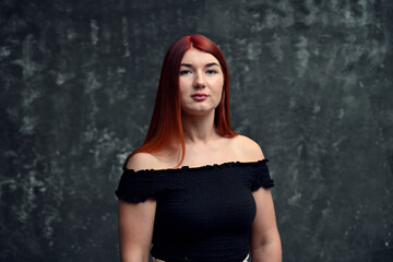 Fototapeta premium Portrait of a red-haired Caucasian girl model with long hair on a gray background looking directly at the camera