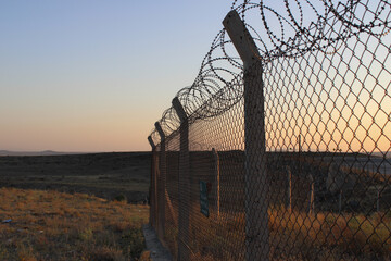 Barbed wire on sunset. Spiky wire fence. Prison barbed fence. Airport security fence after sunset. National border. Barbed Wire Fence in a military base. Area with barbed wire. Dangerous area.