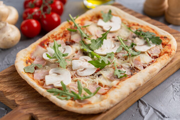 Rectangular pizza with mushrooms, tomatoes and arugula on a wooden cutting board