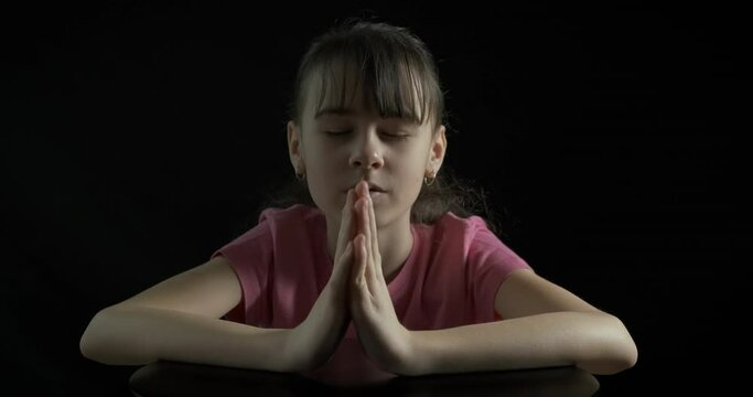 Meditating with namaste hands. A child close her eyes and meditate in the room on the black background.