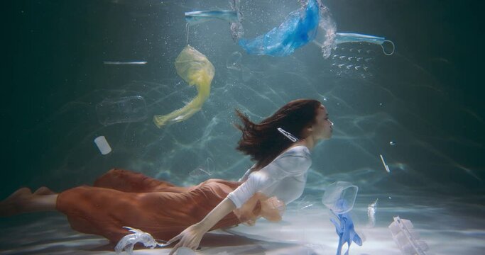 Young tourist woman swims surrounded by single use plastic waste trash polluting all around under water slow motion.