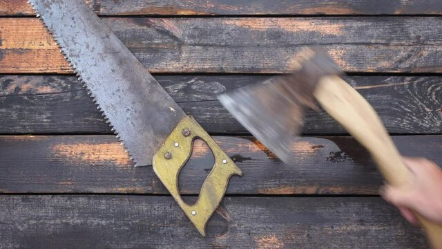 Close-up top view 4k stock video footage of old used vintage tools laying on wooden floor. Man takes old rusty saw and axe one by one from weathered wooden surface background