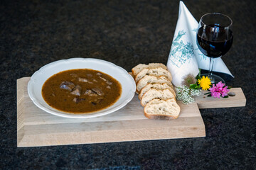 fresh cooking at home and ready to eat, the innards from a roebuck for a goulash on a wood board with sliced bread and a glas of red wine