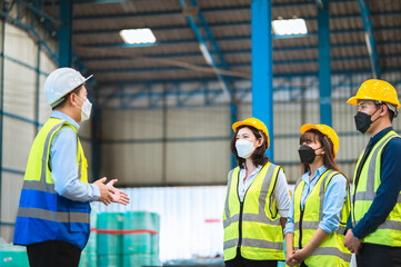 The factory employee consists of engineers, foreman, technicians, and related department staff. Wear a mask, hard hat, and vest. meeting before starting work inside the warehouse. Teamwork concept.