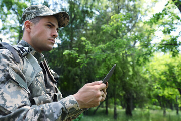 Soldier with backpack using tablet in forest