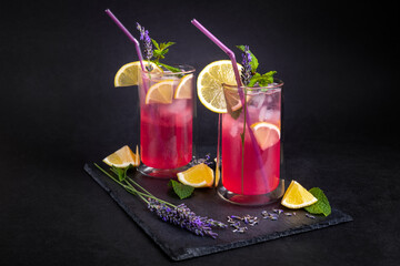 Fresh summer drink with lavender, lemon and mint. Refreshing seasonal beverage, served with ice, on black slate board.