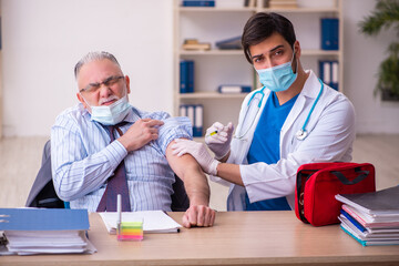 Young male doctor visiting old businessman at workplace