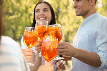 Friends clinking glasses of Aperol spritz cocktails outdoors, focus on hands
