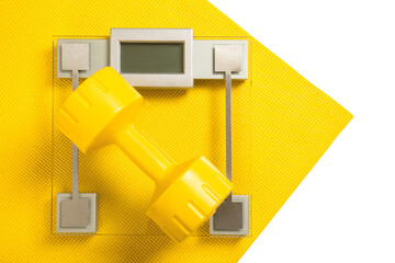 Yellow dumbbell and weight scale on fitness mat