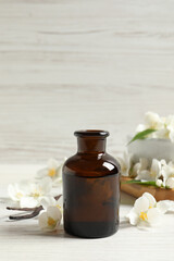 Jasmine essential oil and fresh flowers on white wooden table
