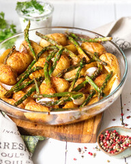 European cuisine. Baked potatoes with asparagus with olive oil. A delicious dish is served with cream sauce and herbs. Fresh crop of vegetables on a white wooden background.