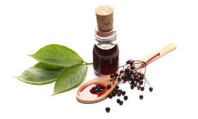 Squeezed elderberries juice, syrup in glass bottle with wooden spoon and green leaves and berries...