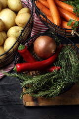 Raw potatoes, carrots, onion, garlic, chili peppers, thyme, rosemary and parsley in metal baskets on the table