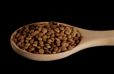 Lentils pile in wooden spoon isolated on black background with clipping path