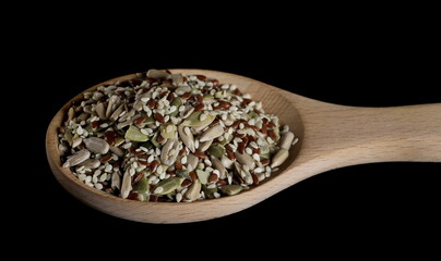 Mixed seeds pile with sunflower, sesame, linseed, pumpkin seed in wooden spoon isolated on black background