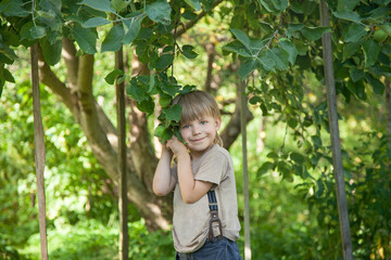 a little boy with a dirty face holds his hands to the branches of an apple tree in the garden.