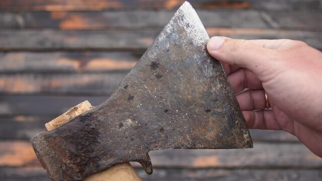 Close-up view 4k stock video footage of adult male hand holding old rusty axe tool isolated on brown weathered wooden background. Man touches blade of axe