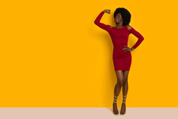 Confident Young Black Woman In Elegant Red Mini Dress Is Standing And Flexing Biceps