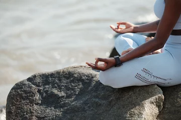 Wandcirkels plexiglas Close-up beeld van een fitte vrouw die in de lotuspositie zit en geniet van haar kalme meditatie op het strand © DragonImages