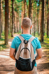 Naklejka premium A young man with a backpack walks through a pine summer forest