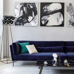 Stylish and modern living room interior with blue velvet sofa, mock up paintings, design black lamp, plant, table, decoration, concrete floor, elegant personal accessories in home decor.